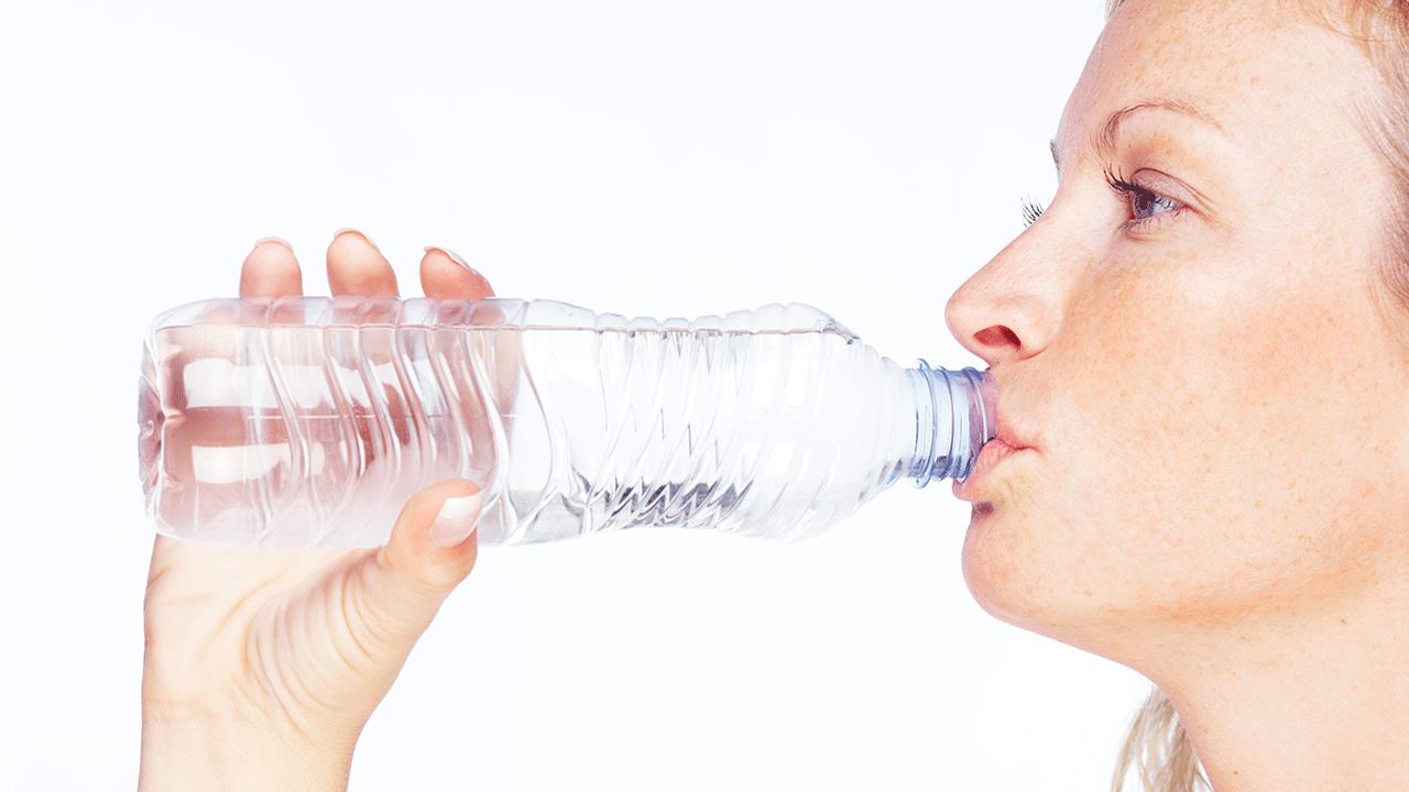 Close-up af nordisk kvinde, der drikker vand af klar plastikflaske på hvid baggrund.  