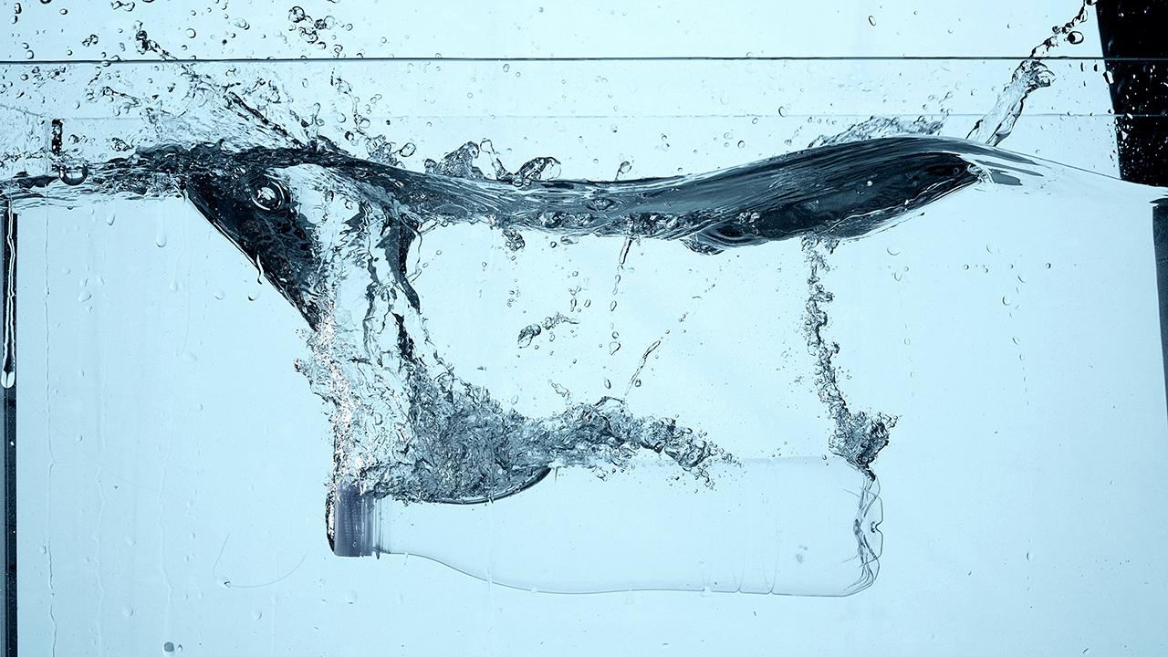 Køligt, blåligt billede af tank med vand, hvor vandet brydes af klar plastikflaske.