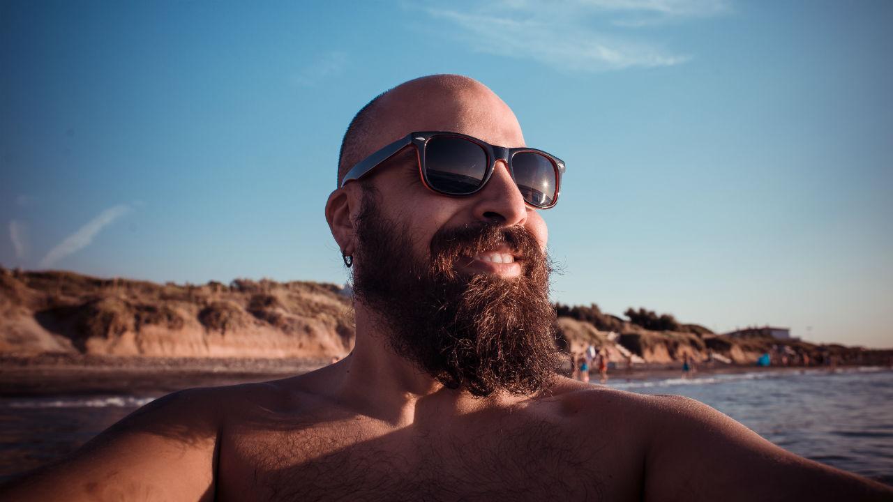 Mand med stort skæg og solbriller på strand.