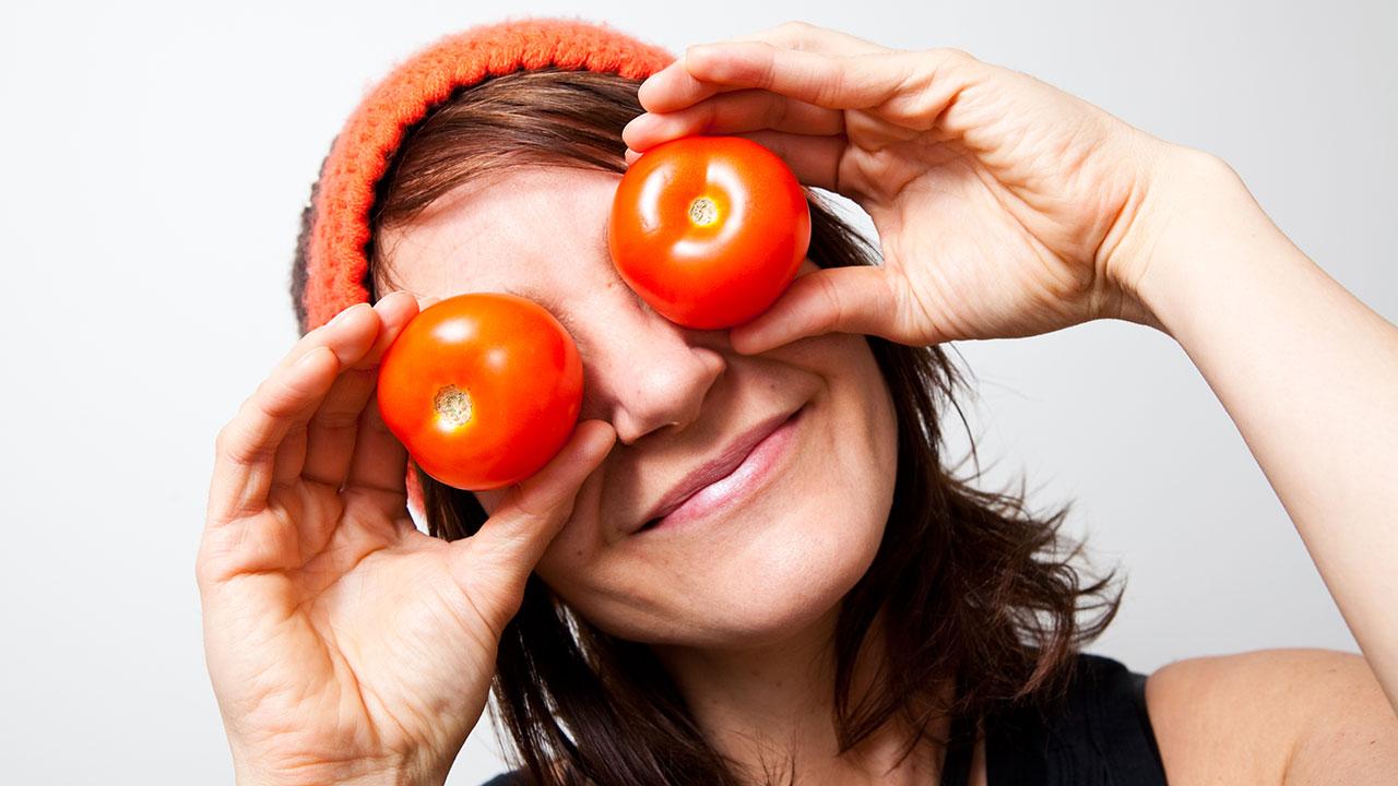 Kvinde holder tomater op foran sine øjne og smiler