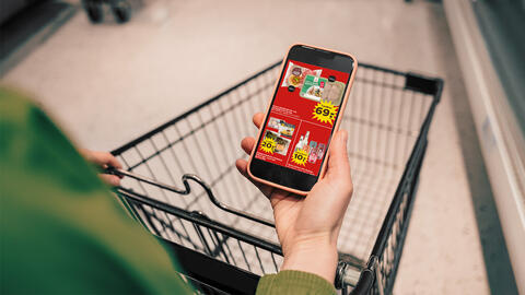 Hånd med tilbudsavis i hånden ved indkøbsvogn