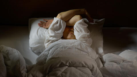 kvinde med hovedpine ligger i sengen i mørkt rum 