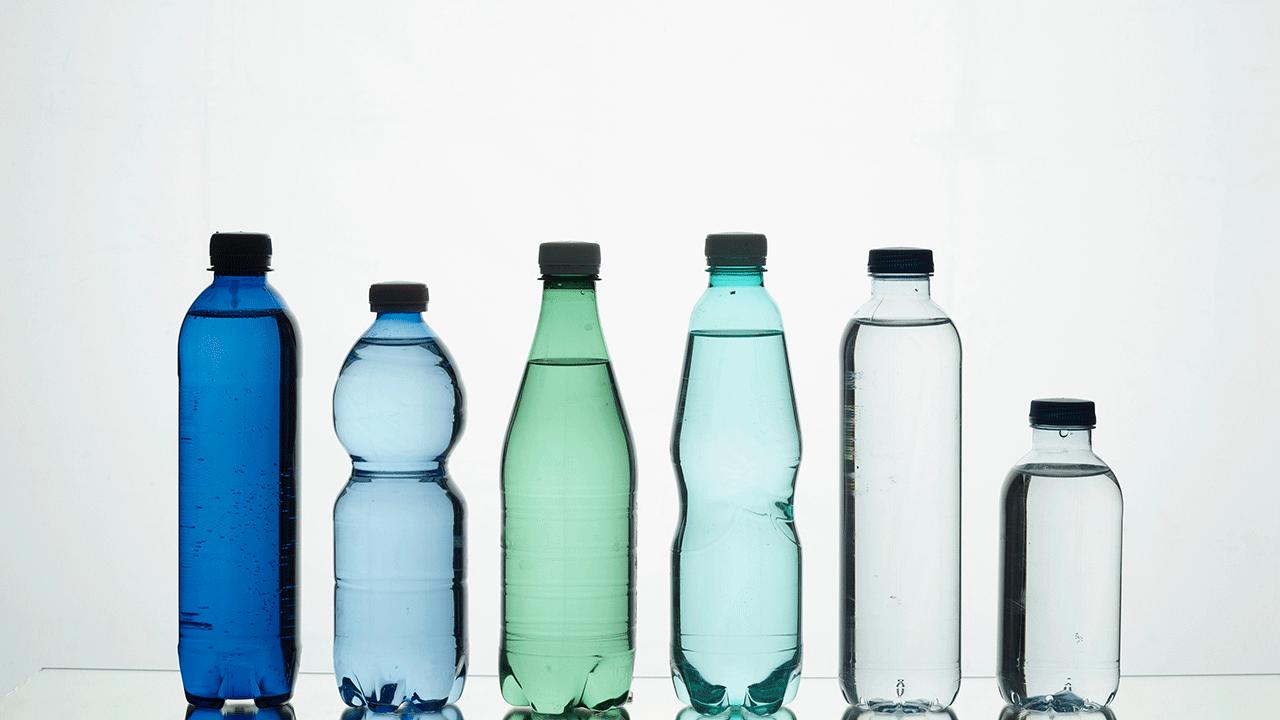 Seks plastikflasker med vand i forskellige farver og størrelser på lys baggrund. 