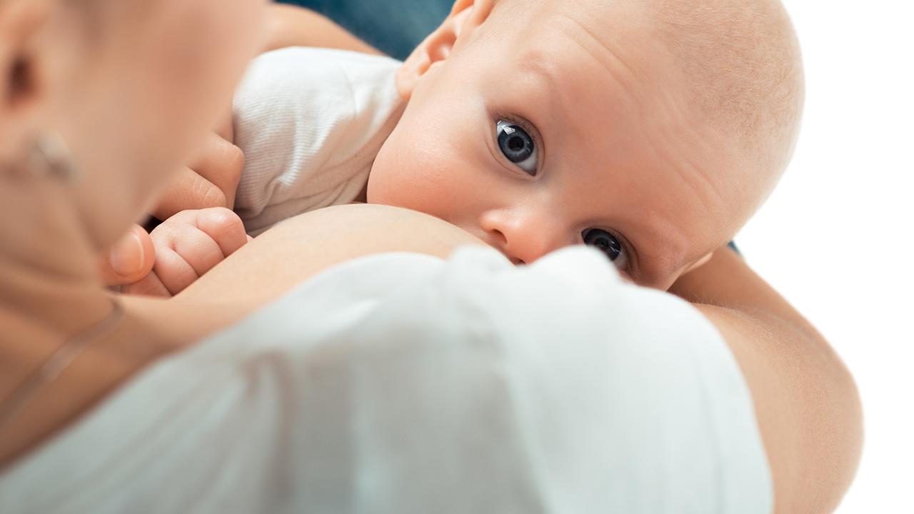 Spædbarn bliver ammet fra højre bryst, mens den kigger ind i kameraet.