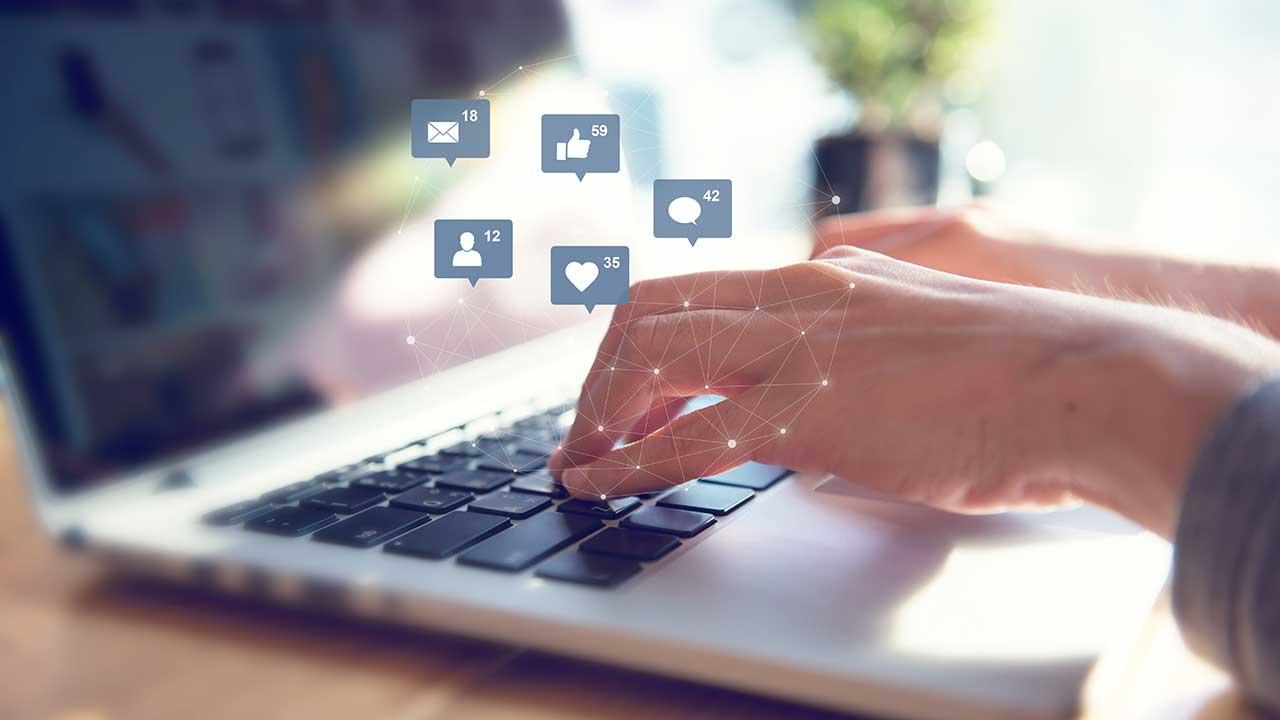 Hænder på computertastatur med ikoner fra sociale medier. 