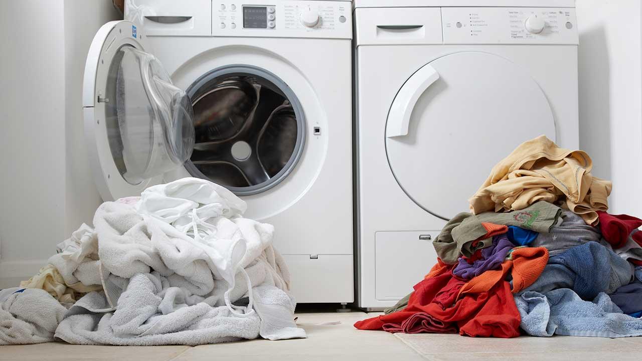 Hvid vasketøjsbunke foran hvid vaskemaskine med åben låge, og kulørt vasketøjsbunke foran hvid tørretumbler med lukket låge.