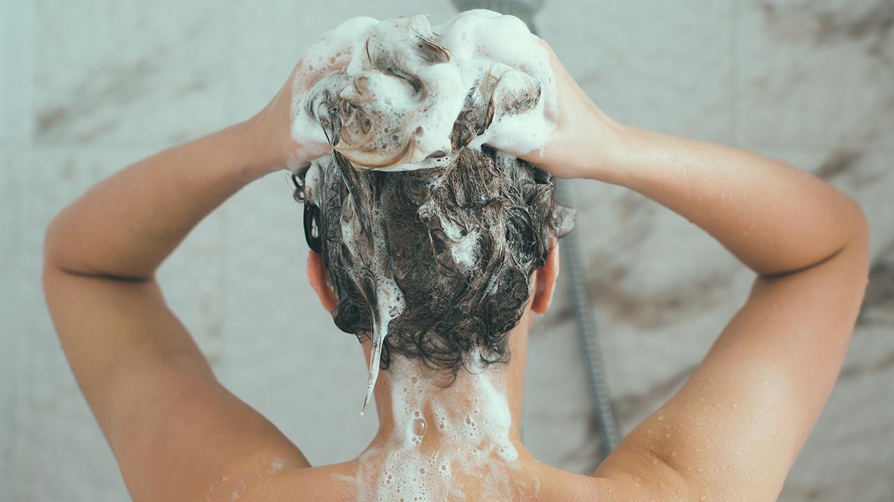 Ung kvinde vasker hår med meget skummende shampoo