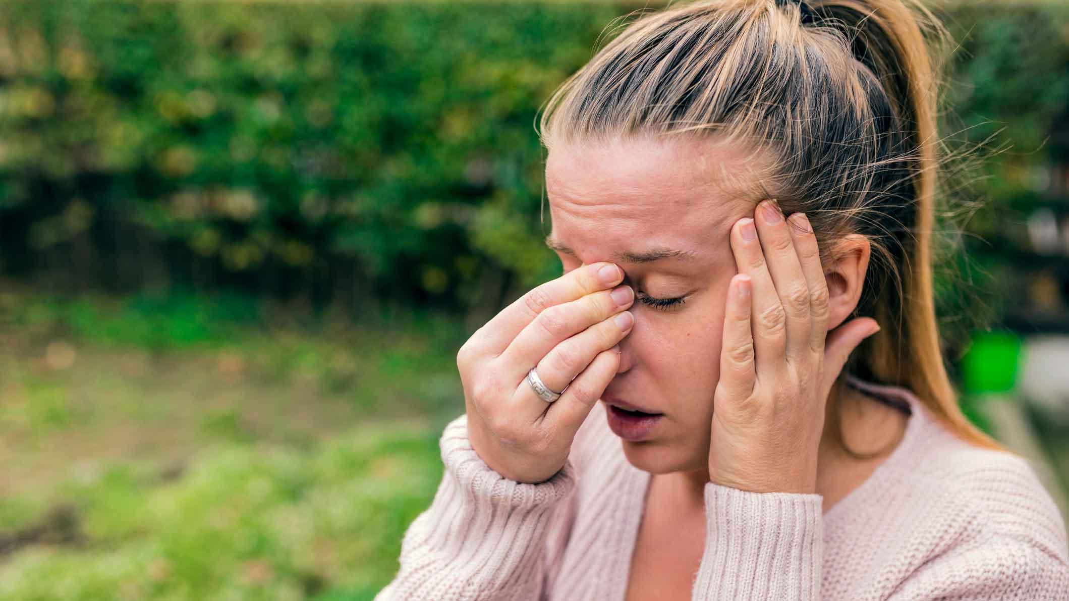Kvinde plaget af allergi tager sig til næseryggen og tindingen