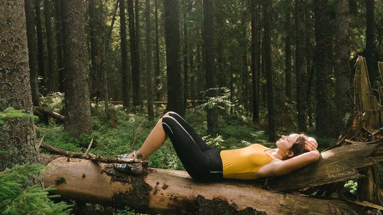 Kvinde ligger på et væltet træ i skoven og nyder roen