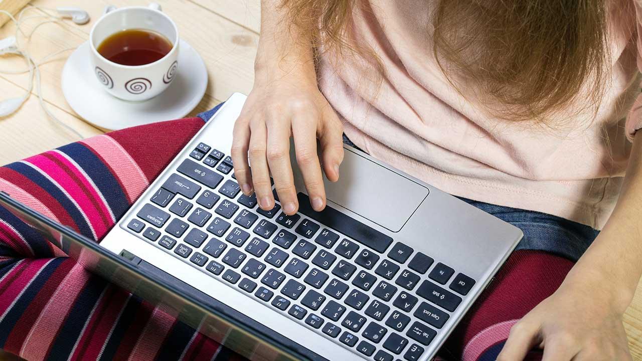 En pige sidder med sin laptop i skødet 