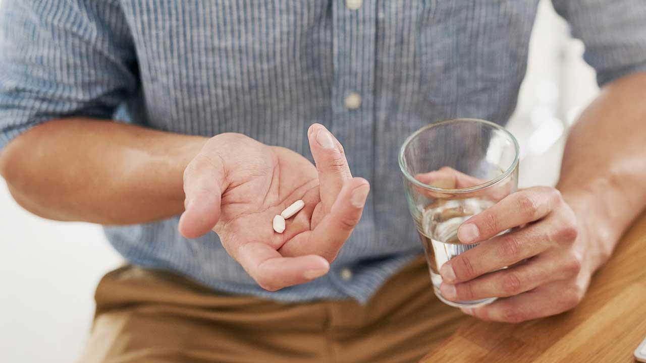En mand holder to piller i den ene hånd og et glas vand i den anden 