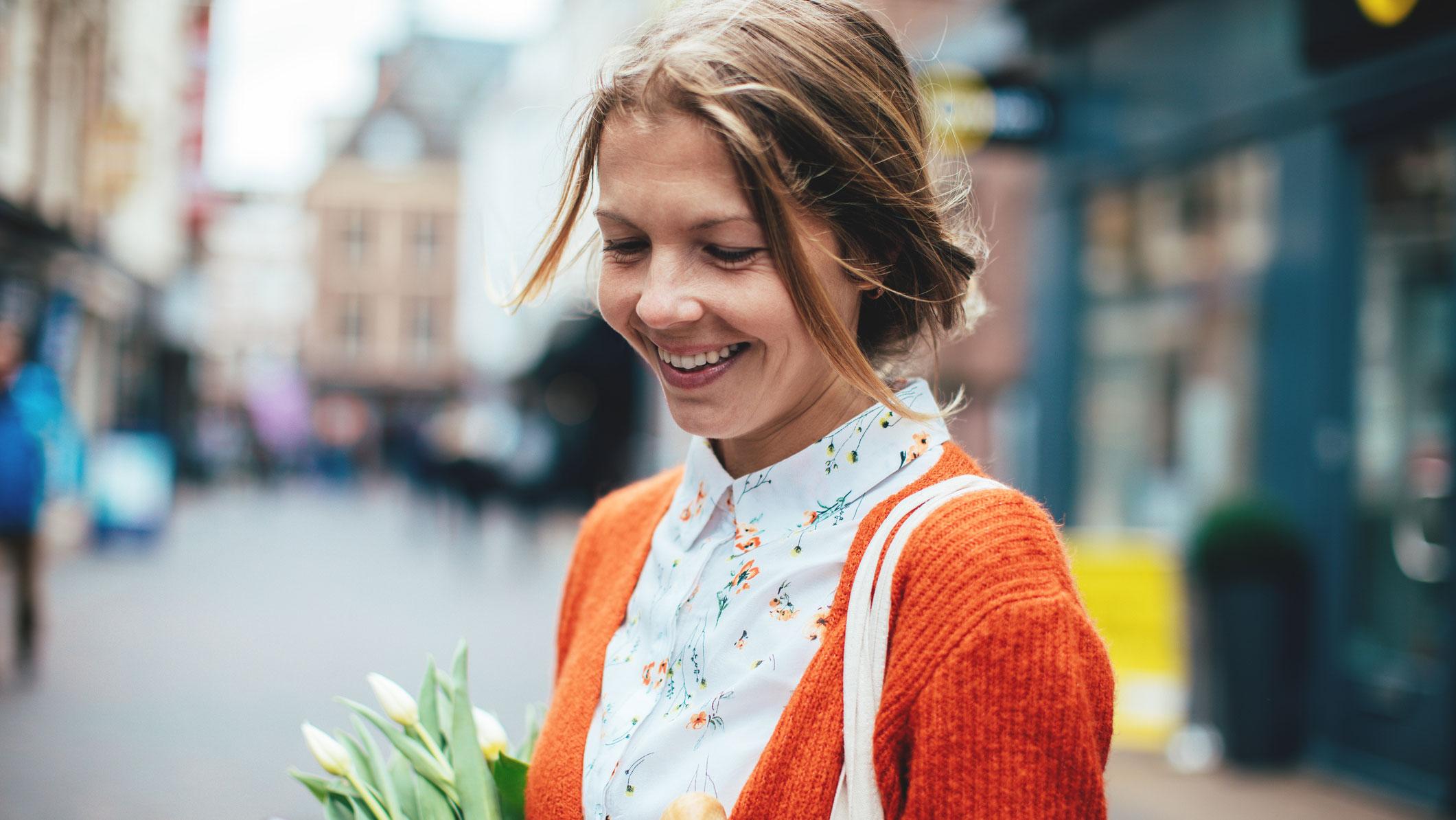 Optimistisk kvinde med blomster i favnen smiler og kigger ned