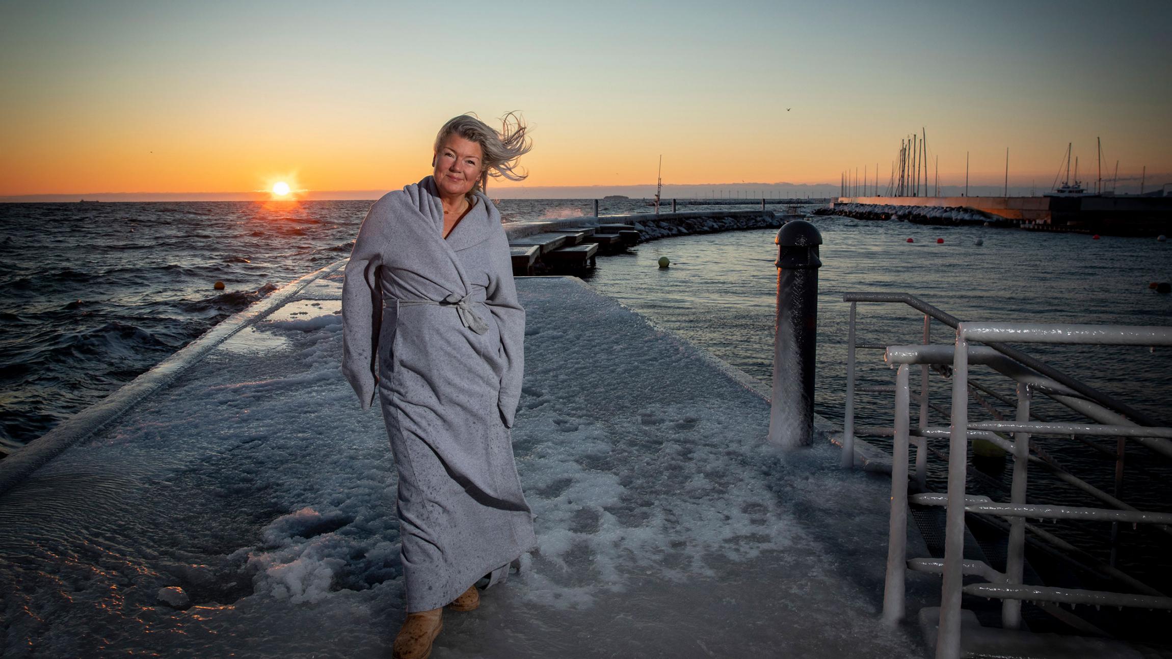 Kvinde i badekåbe på isdækket badebro foran solnedgang
