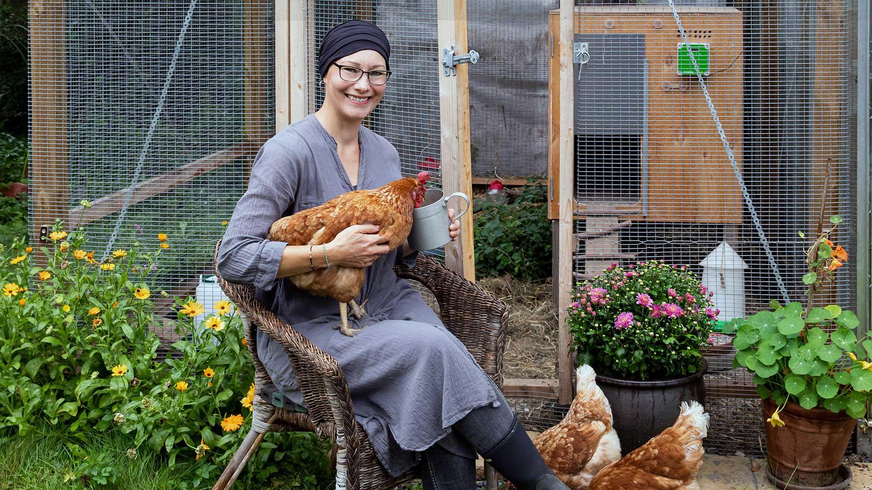 Tina sidder med høne på skødet foran hønsehus