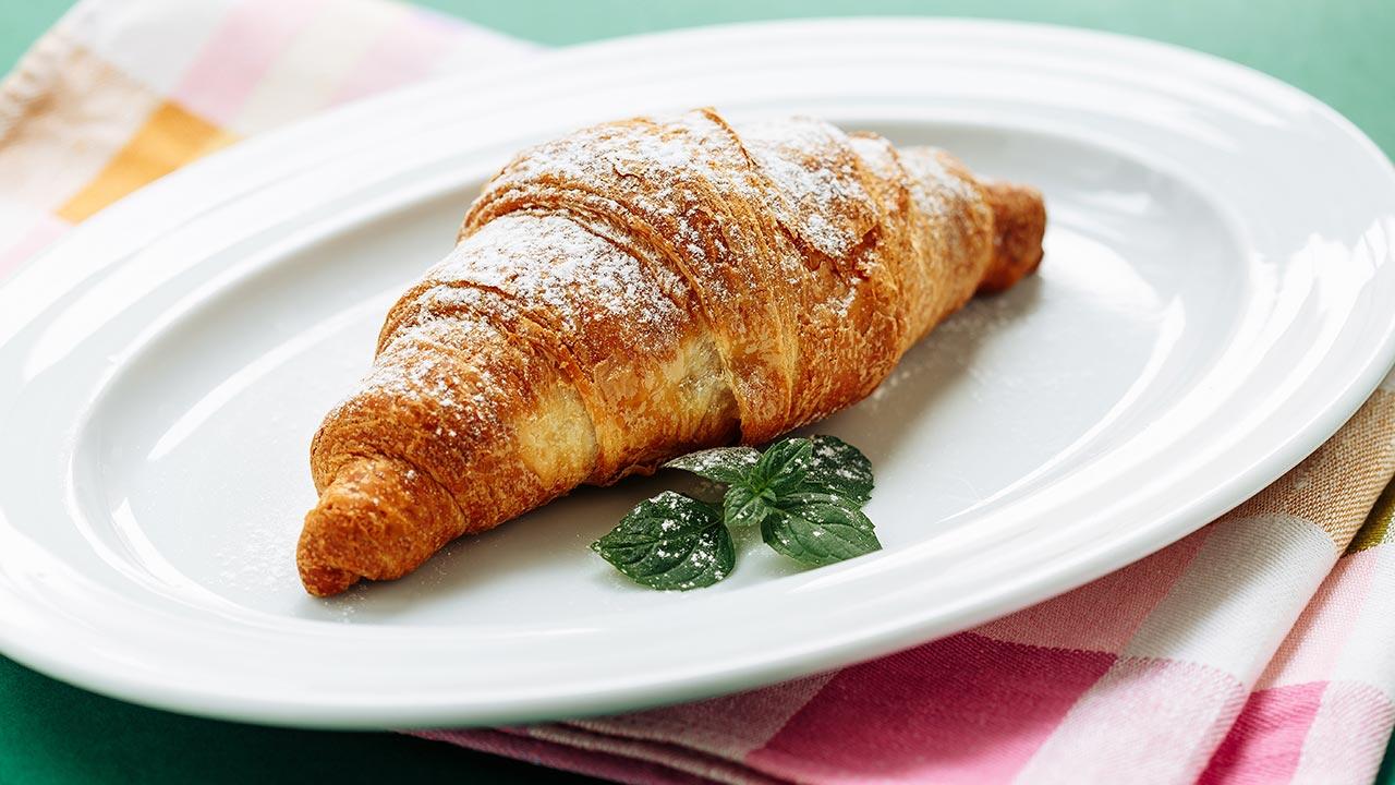 En croissant ligger på en hvid tallerken og frister