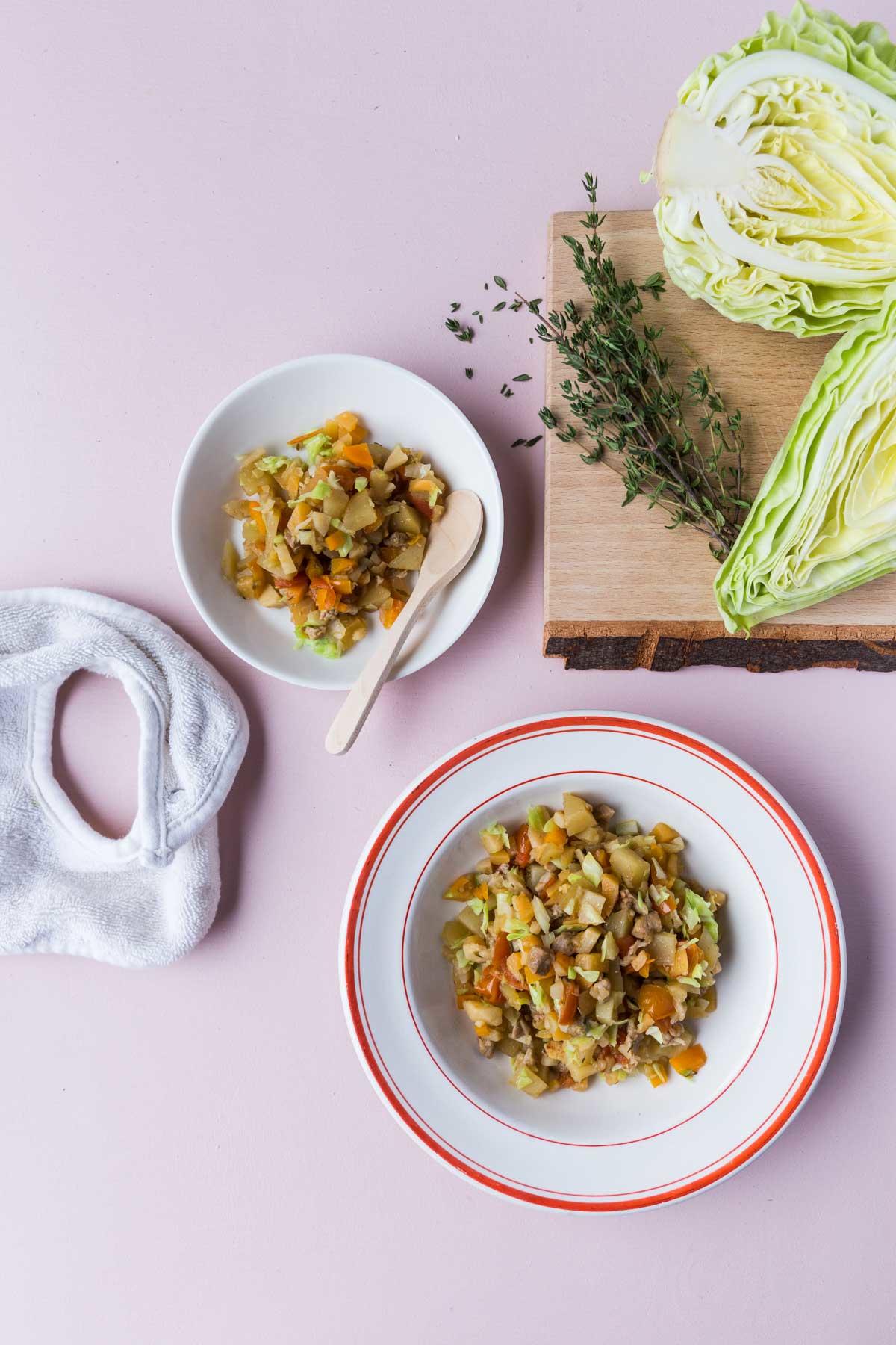 Simreret med gris og kål i to tallerkener på et bord med grøntsager
