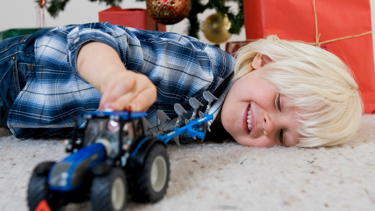 Dreng leger på gulvet med en traktor foran juletræet juleaften