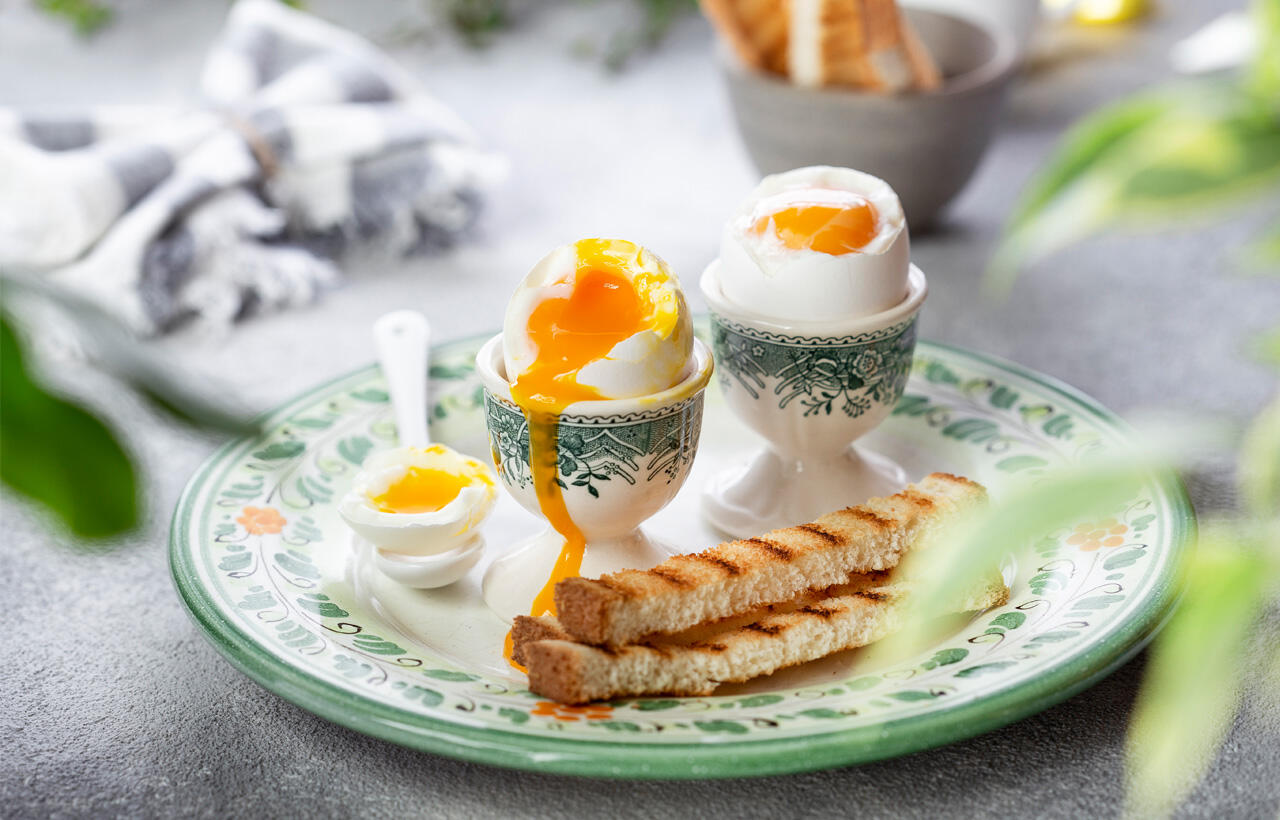 Blødkogt æg i æggebærer på tallerken med brød.