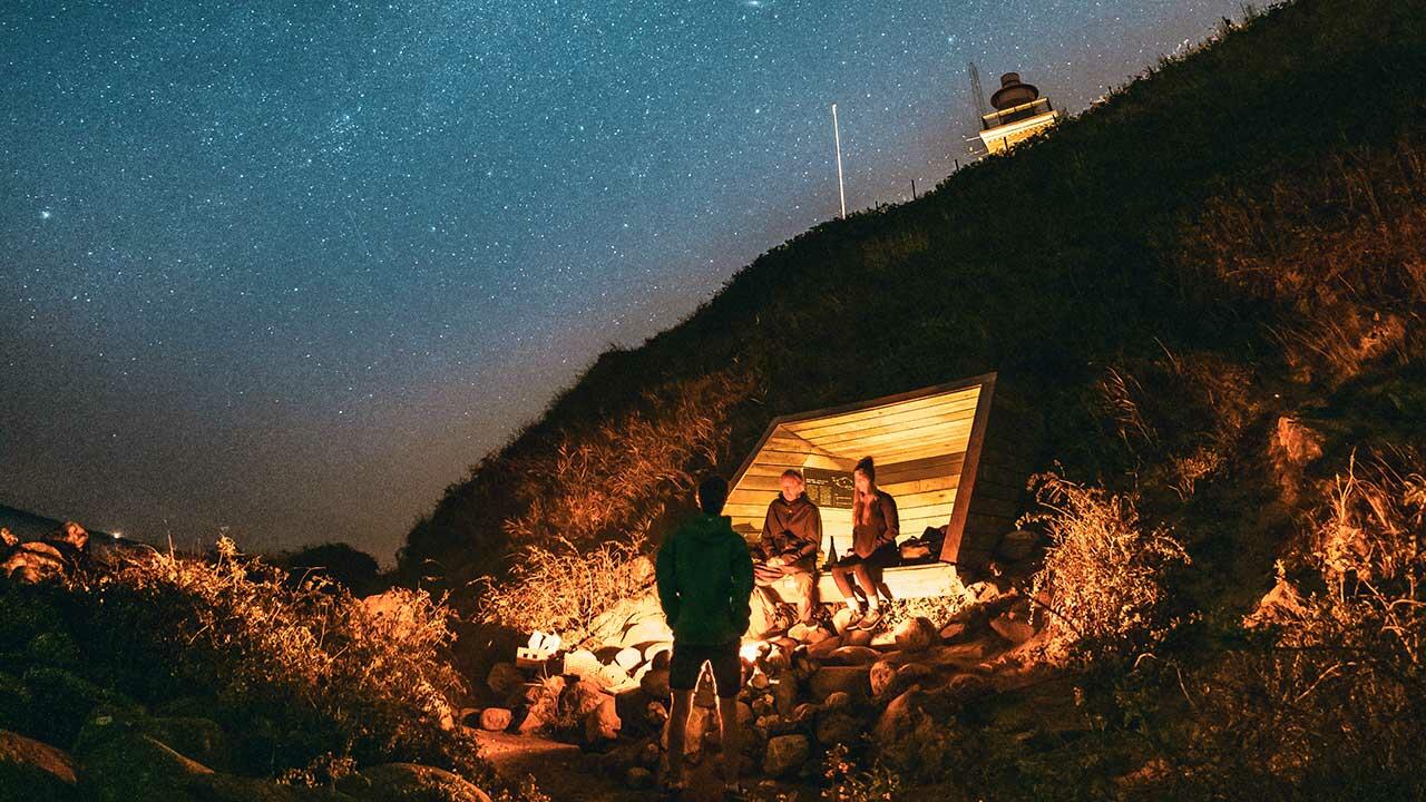 Shelter ved Røsnæs Fyr med stjernehimmel og fyr i baggrunden  