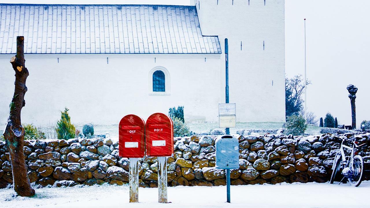 2 postkasser står i sneen ved vejkant foran kirke