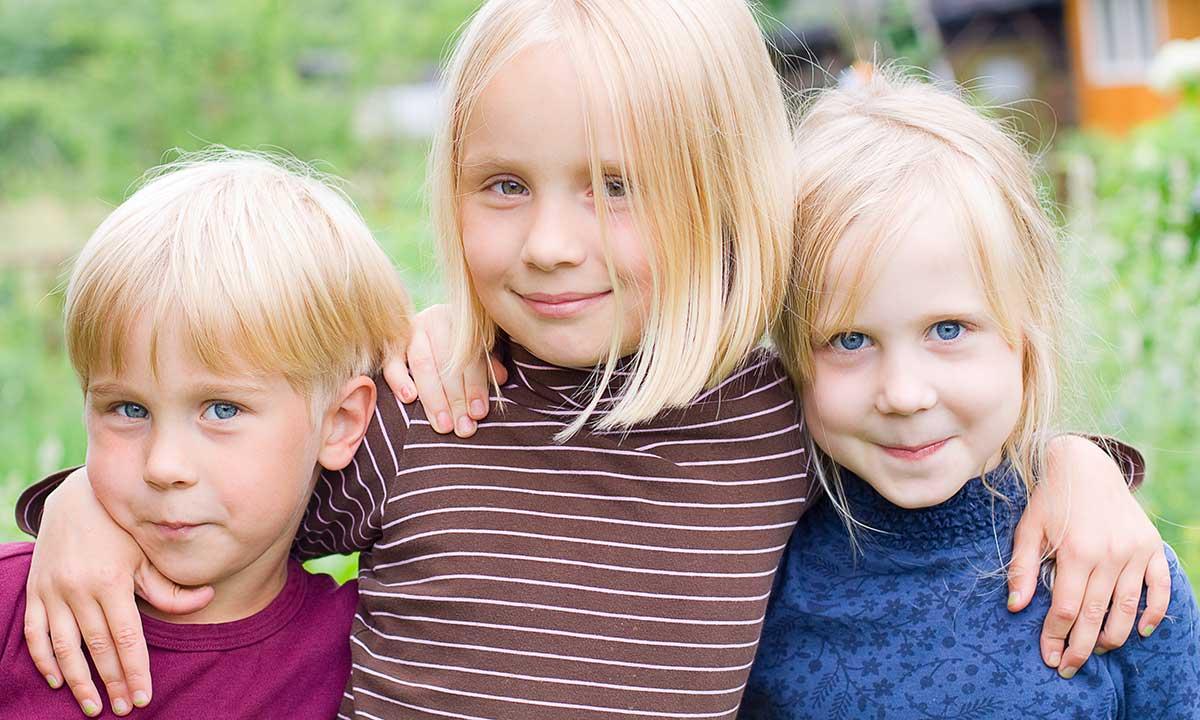 Tre børn står ved siden af hinanden og smiler ind i kameraet
