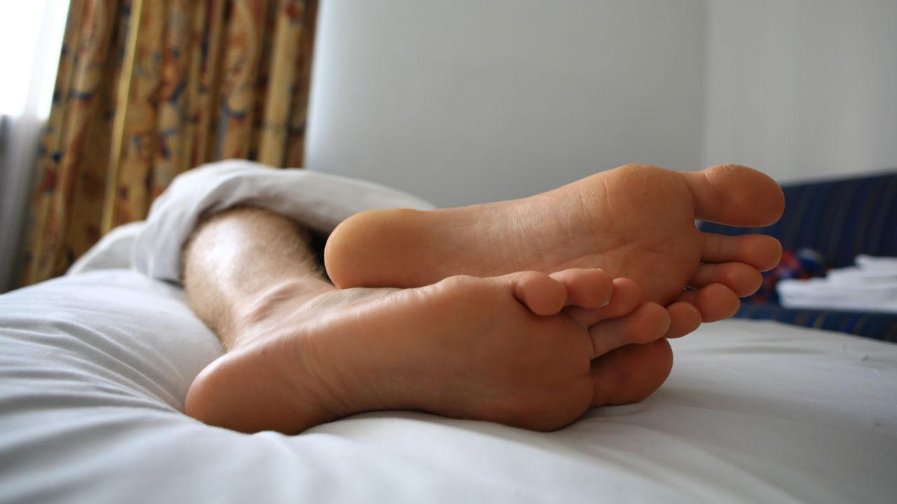 Mand ligger med kun fødderne i sengen.